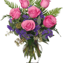 Pink roses in a clear glass vase with purple filler flowers