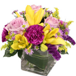 Mixed bouquet of yellow lilies, pink roses, and purple flowers in a glass vase