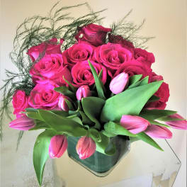 Compact arrangement of hot pink roses and tulips in a square glass vase