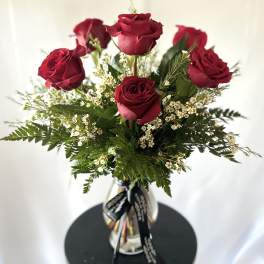 Red roses arranged in a clear glass vase with white filler flowers