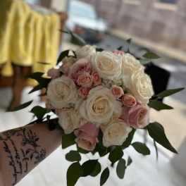 Handheld bouquet of white and blush roses with greenery