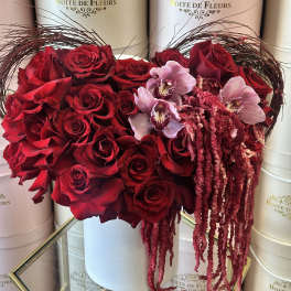 Heart-shaped box of red roses with pink orchids and trailing amaranthus
