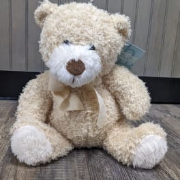 Cream teddy bear with a ribbon bow sitting on a wooden floor