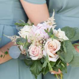 Handheld bouquet of pale pink and white roses with greenery