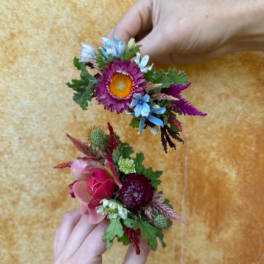 Two small floral wrist corsages held in hands against a warm background