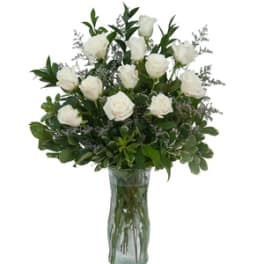 Tall arrangement of white roses with lush foliage in a clear glass vase