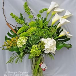 Green and white floral arrangement in a clear glass vase with calla lilies