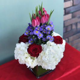 Bouquet of red roses, white hydrangeas, purple daisies, and pink tulips in a glass vase