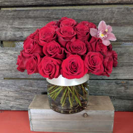 Red rose bouquet in a clear glass vase with a pink orchid accent