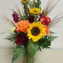 Mixed bouquet with sunflowers, roses, and carnations in a glass vase