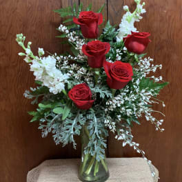 Red roses and white flowers arranged in a clear glass vase.