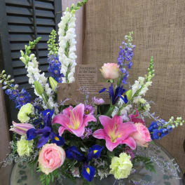 Pink lilies and roses with blue and white flowers in a low arrangement