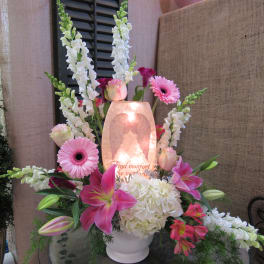 Pink lilies and gerbera daisies arranged around a glowing memorial candle.