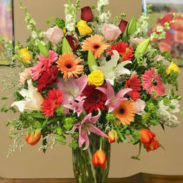 Mixed bouquet of roses, lilies, and gerbera daisies in a tall glass vase
