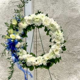 White floral wreath on a stand with blue ribbon accents