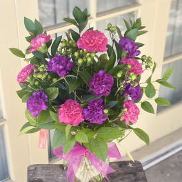 Pink and purple carnations in a glass vase with a pink ribbon