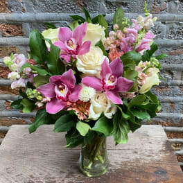 Vase arrangement of pink orchids, white roses, and pastel blooms in a clear glass cylinder