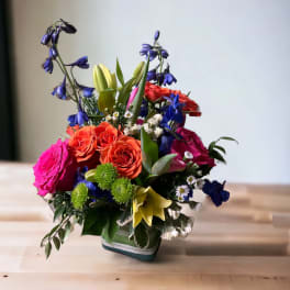 Colorful mixed bouquet in a square vase with roses and lilies