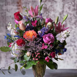 Mixed bouquet of roses, lilies, and purple flowers in a glass vase