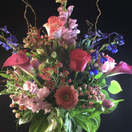 Tall mixed bouquet in a glass vase with pink, purple, and red blooms