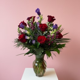 Red roses and purple flowers in a clear glass vase