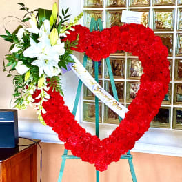 Heart-shaped red floral wreath on an easel with white lilies and a ribbon