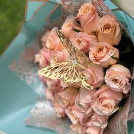 Bouquet of pale peach roses wrapped in turquoise paper with a butterfly pick