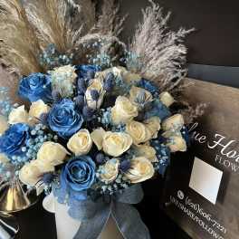 Blue and cream roses arranged in a white hatbox with a ribbon.