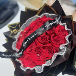 Bouquet of red roses wrapped in black paper with a birthday ribbon