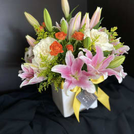 Pink lilies and white roses in a white vase with a yellow ribbon