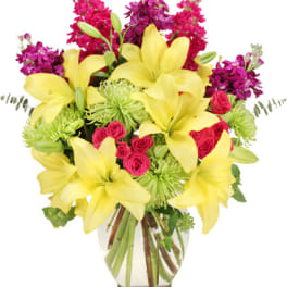 Bouquet of yellow lilies, pink roses, and purple flowers in a glass vase