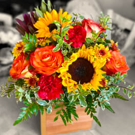 Bright mixed bouquet with sunflowers, roses, and carnations in a wooden box