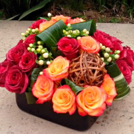Red and orange roses arranged in a low black container with woven accents