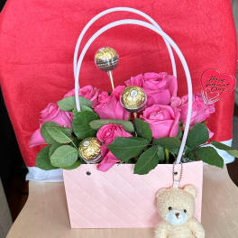 Pink roses in a gift bag with chocolates and a teddy bear charm