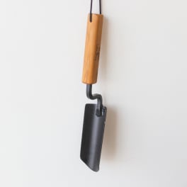A hanging metal tool with a wooden handle against a white wall.