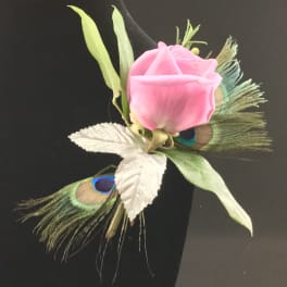 Pink rose boutonniere with peacock feathers and white leaves