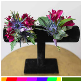 Two magenta corsages with blue thistle on a black stand