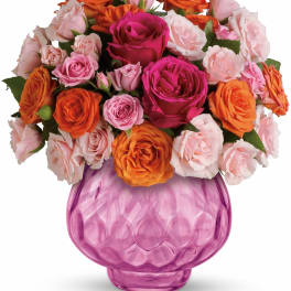 Round arrangement of pink and orange roses in a faceted pink glass vase