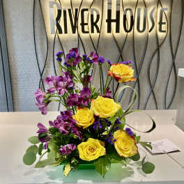 Yellow roses and purple flowers arranged in a low centerpiece