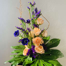 Tall bouquet of peach roses and purple flowers with large green leaves