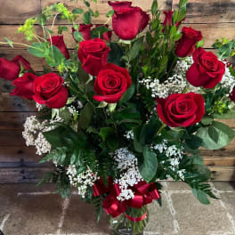 Red roses in a glass vase with white filler flowers and a red ribbon