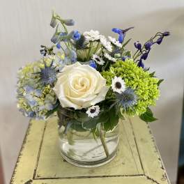 White rose arrangement with blue flowers in a clear glass vase