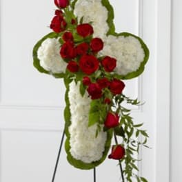 Cross-shaped floral tribute with red roses and white flowers on a stand