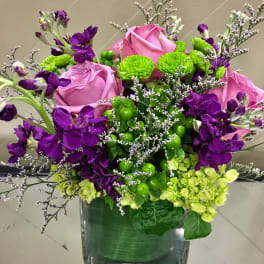 Pink roses and purple flowers arranged in a square glass vase