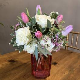 Pink tulips and white roses arranged in a red glass vase