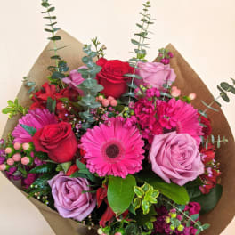 Bouquet of pink and red roses with gerbera daisies in brown paper