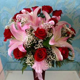 Red roses and pink lilies arranged in a tall vase with baby's breath