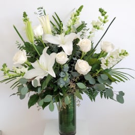 White lilies and roses in a tall green glass vase
