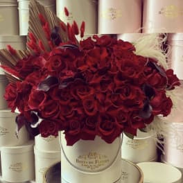 Red rose arrangement in a round hat box with decorative feathers