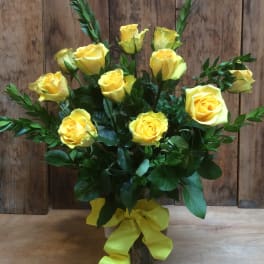 Yellow roses arranged in a glass vase with a yellow ribbon